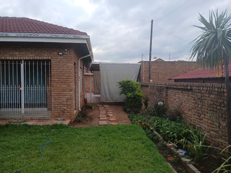 Rear garden area featuring a brick boundary wall with electric fencing, a paved pathway, and a security gate leading to the main house structure.