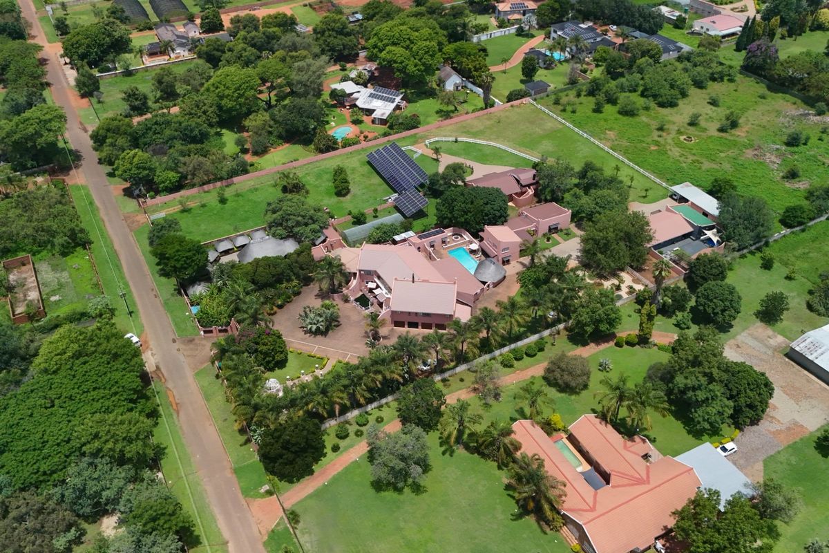 Aerial view of a large farm property featuring multiple buildings, a swimming pool, extensive landscaped grounds, and solar panel installations.