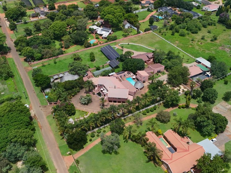 Aerial view of a large farm property featuring multiple buildings, a swimming pool, extensive landscaped grounds, and solar panel installations.