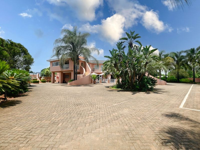 A spacious paved driveway leading to the front facade of a multi-level farm property featuring a distinctive curved staircase and balcony.