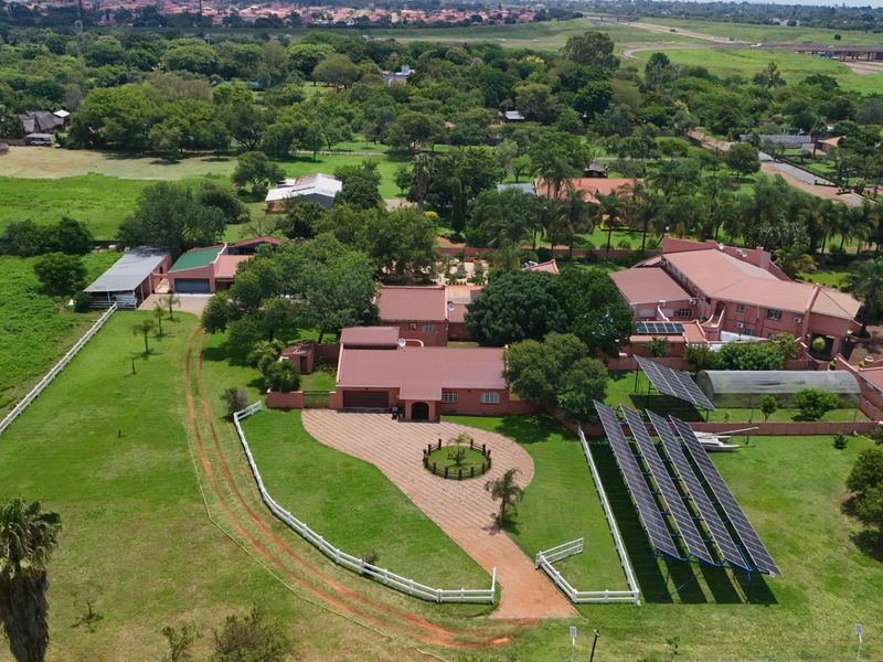Aerial view of a sprawling farm property featuring multiple buildings, a large solar panel array, extensive lawns, and a paved driveway entrance.