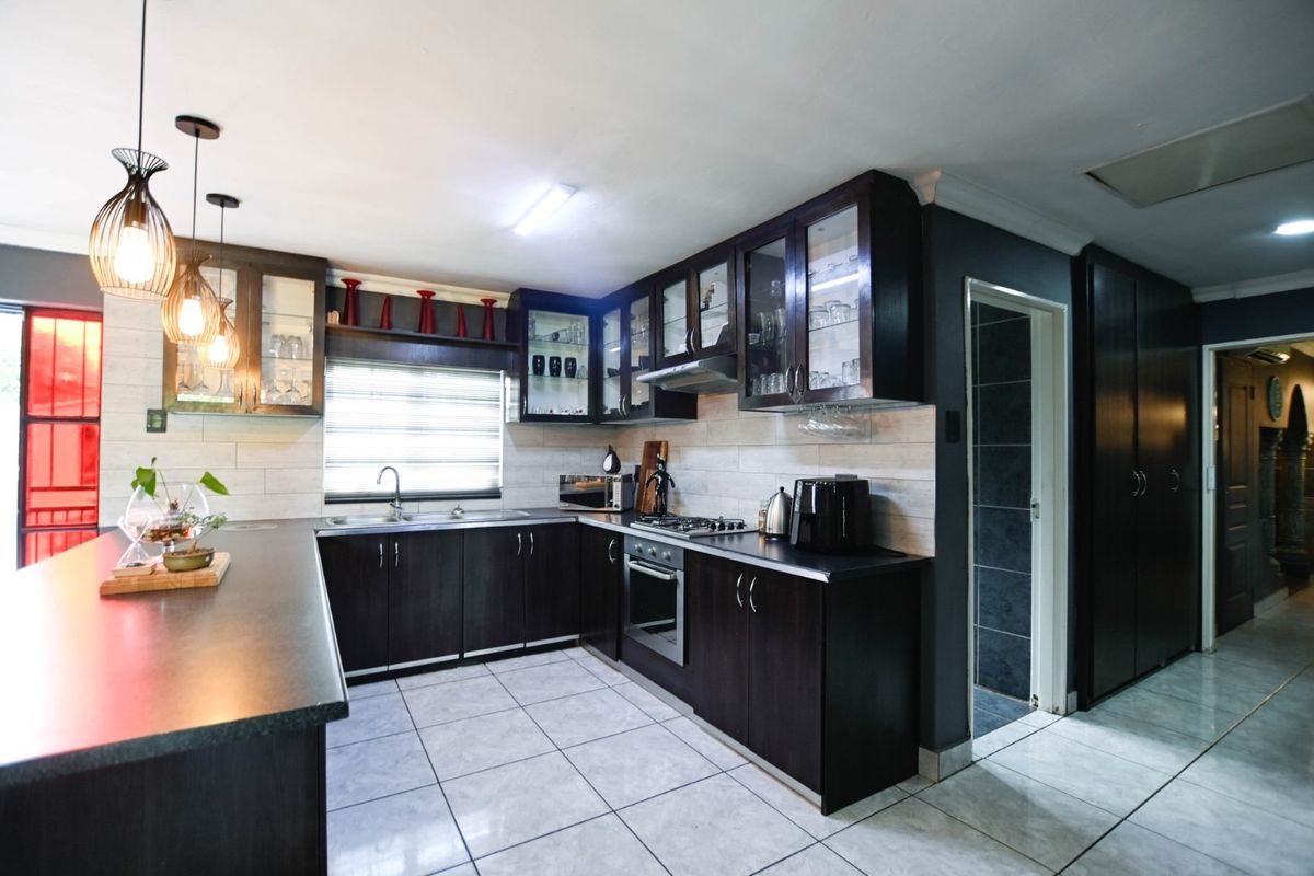 Modern kitchen featuring dark wood cabinetry, stone countertops, integrated gas hob and oven, tiled flooring, and ample storage with glass-fronted display cabinets.