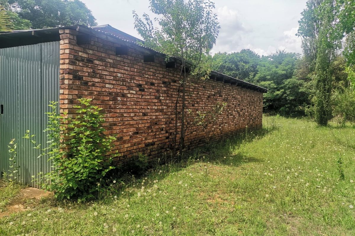 Side view of a rustic outbuilding featuring exposed brickwork and corrugated metal cladding, situated on a large, grassy small holding plot.