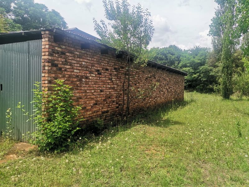 Side view of a rustic outbuilding featuring exposed brickwork and corrugated metal cladding, situated on a large, grassy small holding plot.