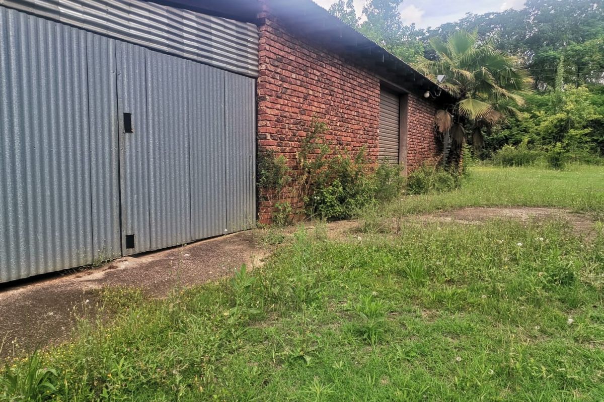 A detached outbuilding or garage featuring exposed brick walls and corrugated metal siding, situated on a large plot with overgrown surrounding grounds.