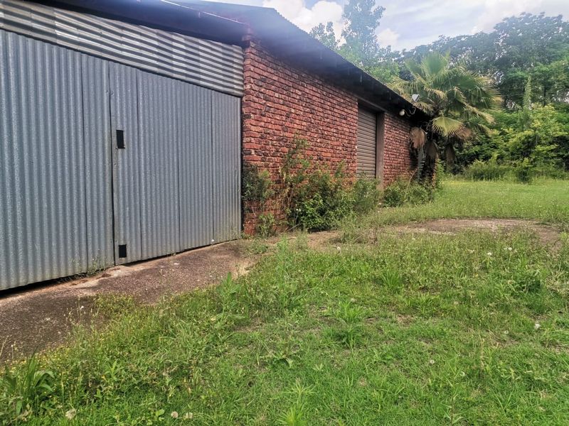 A detached outbuilding or garage featuring exposed brick walls and corrugated metal siding, situated on a large plot with overgrown surrounding grounds.