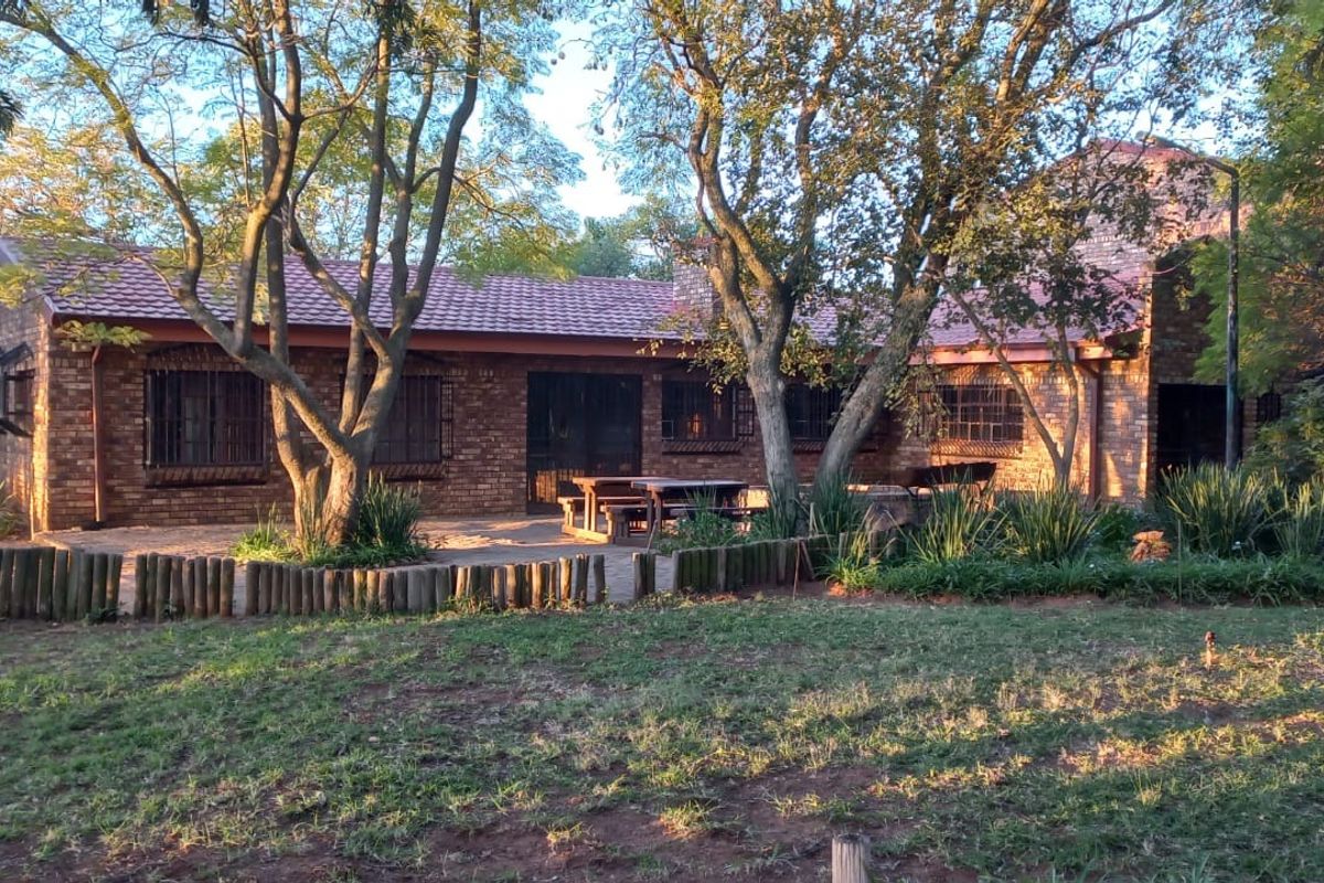 Rear view of a brick farmhouse featuring a tiled roof, security bars on windows, and a paved patio area set within a garden.