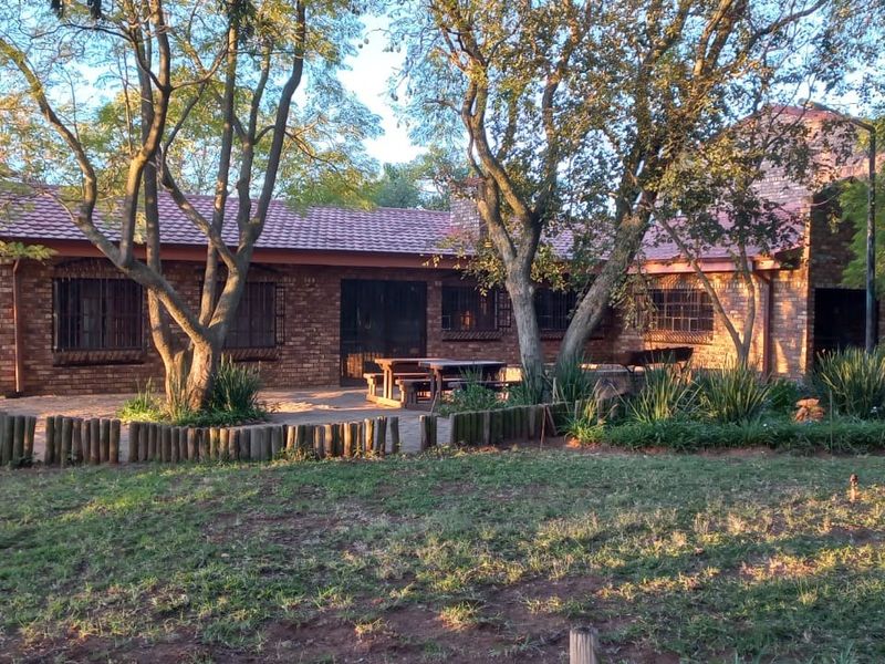 Rear view of a brick farmhouse featuring a tiled roof, security bars on windows, and a paved patio area set within a garden.