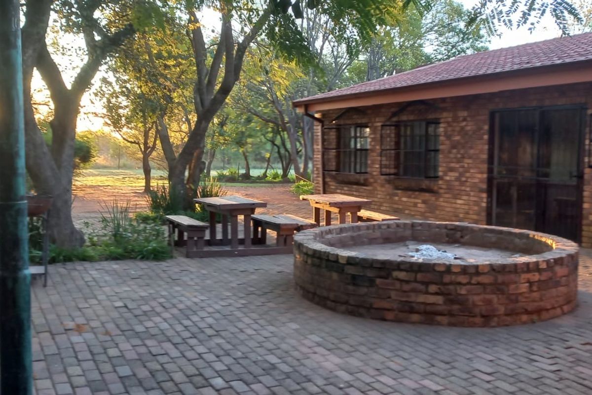 A rustic outdoor patio area featuring brick paving, a built-in circular brick fire pit, and views of the surrounding farm landscape.