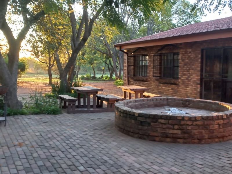 A rustic outdoor patio area featuring brick paving, a built-in circular brick fire pit, and views of the surrounding farm landscape.