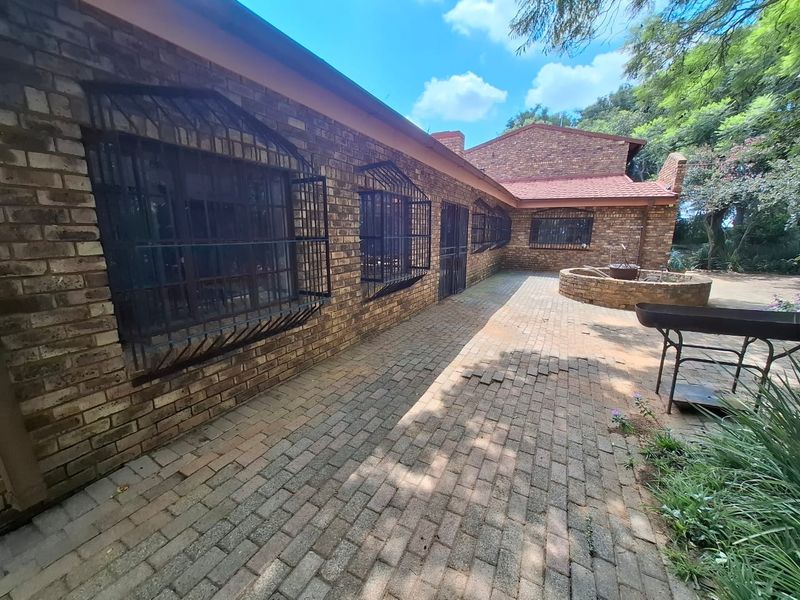 A rear exterior view of a face brick farmhouse featuring a paved patio area, security bars on windows, and a circular brick garden planter.