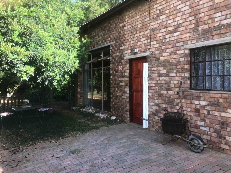 A rear exterior view of a face brick farm building featuring a paved patio area, large glass sliding doors, and a timber entrance door.
