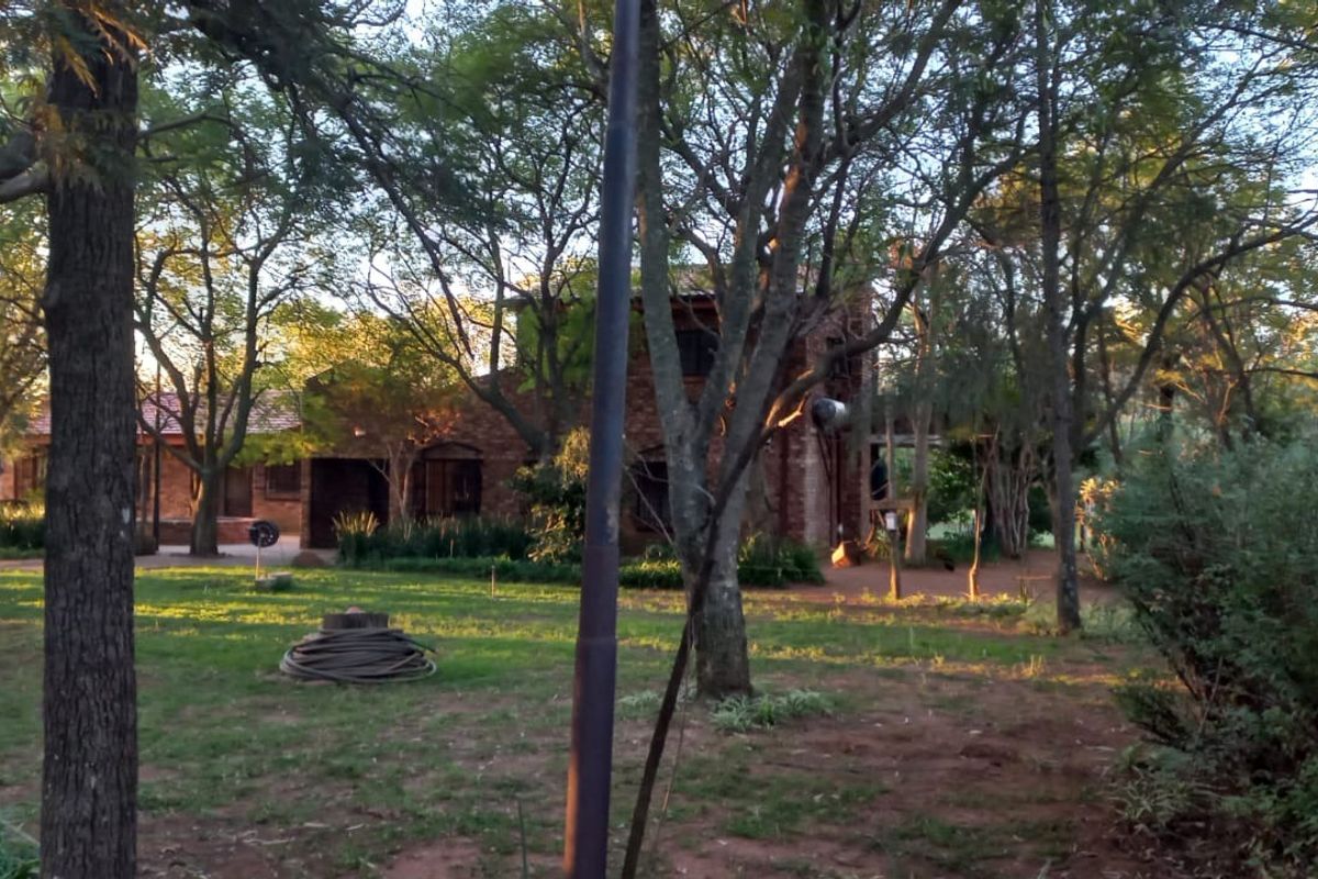 A view of the rear brick farmhouse elevation surrounded by mature trees and a spacious garden area.