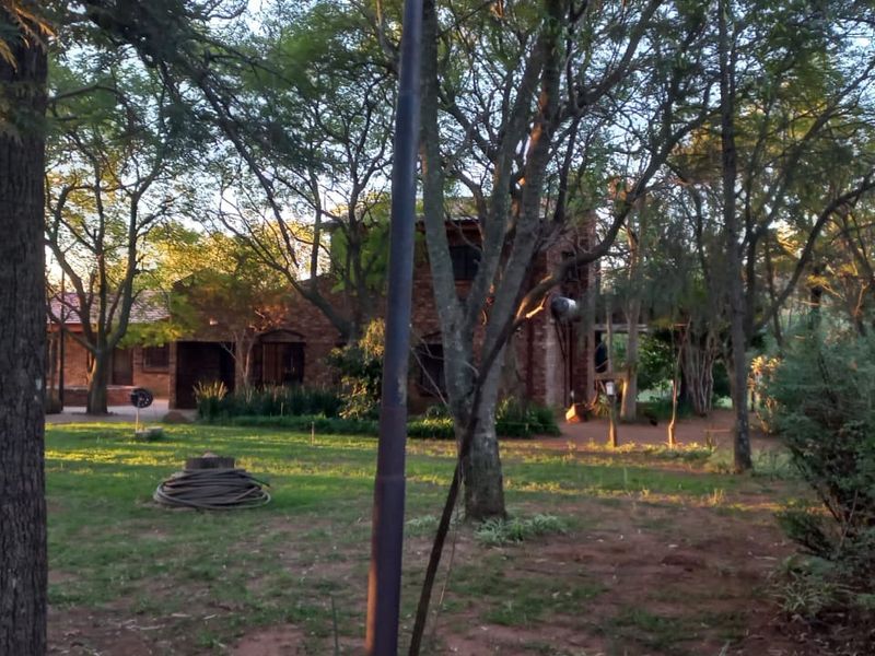 A view of the rear brick farmhouse elevation surrounded by mature trees and a spacious garden area.