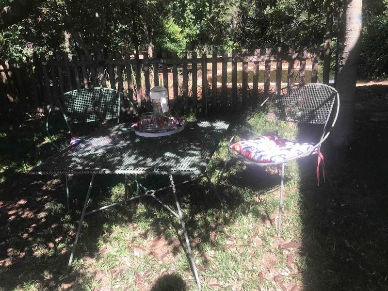 A shaded garden area featuring a wooden picket fence boundary, set within a natural, tree-lined outdoor space.