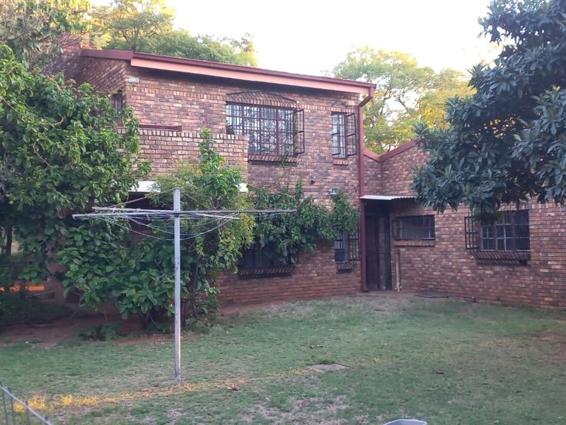 Rear view of a double-story face-brick farmhouse featuring security bars on windows and a surrounding garden area.