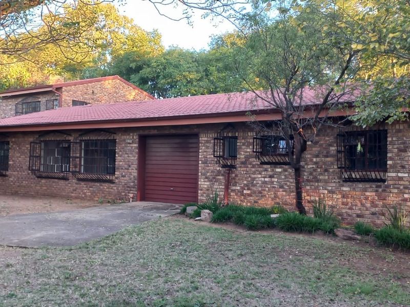 A single-story face brick farm residence featuring a tiled roof, integrated garage, and security bars on windows, set within a mature garden.