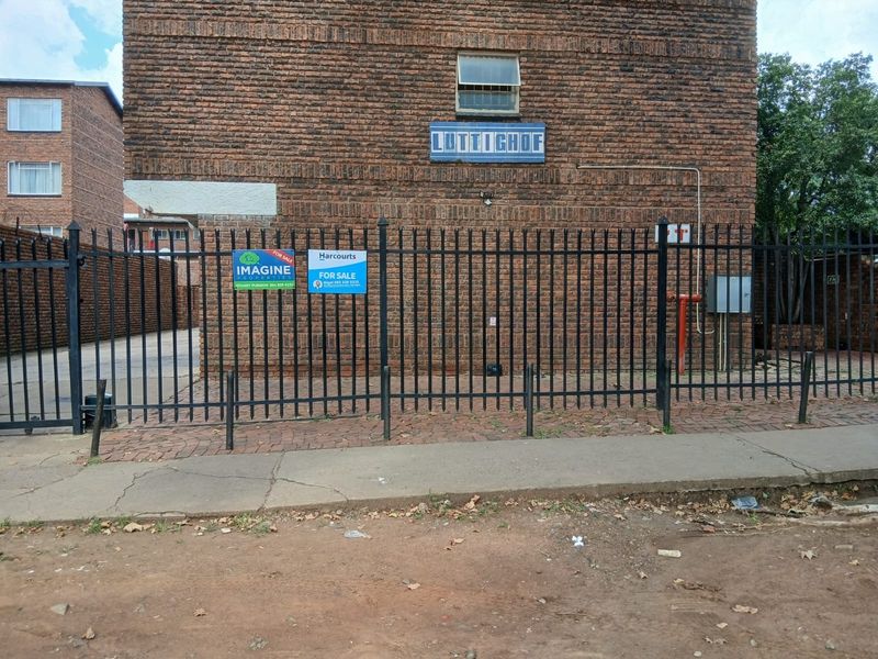 Front exterior view of the Luttighof apartment building featuring brick facade, secure metal fencing, and paved driveway access.