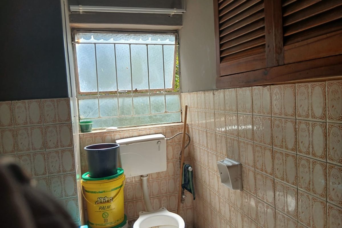 A dated bathroom featuring ceramic wall tiles, a standard toilet with cistern, and a wooden louvered cabinet, requiring modernization and maintenance.