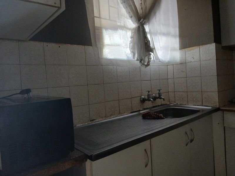 A dated kitchen area featuring a stainless steel sink, tiled splashback, and built-in cabinetry, requiring cosmetic updates to improve functionality and aesthetic appeal.