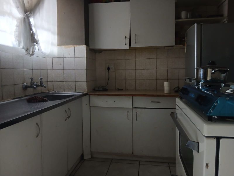 A dated kitchen featuring white cabinetry, tiled backsplash, and a stainless steel sink, requiring modernization to improve functionality and aesthetic appeal.