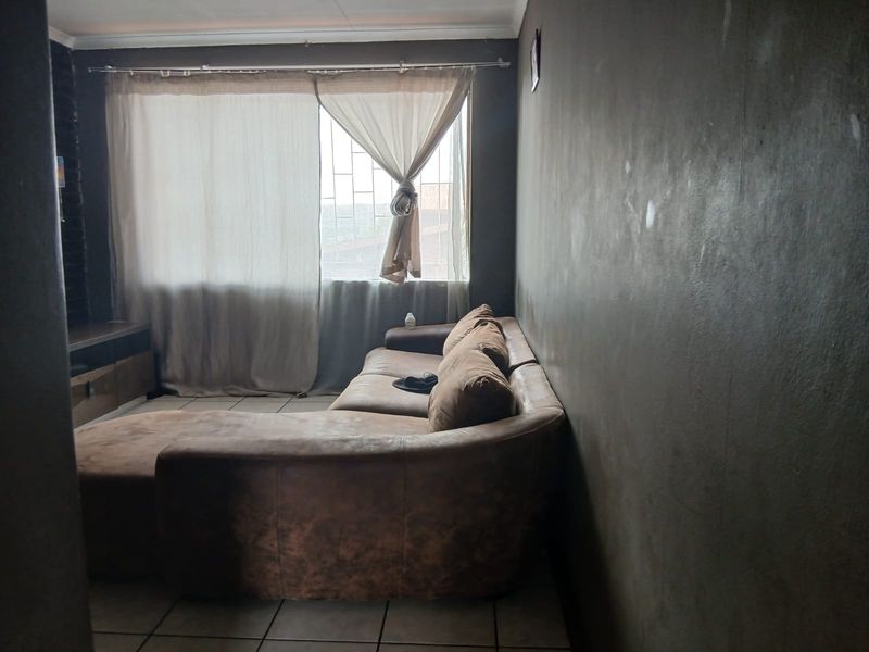 A living room featuring tiled flooring and a window with security bars, currently finished with dark, textured wall paint.