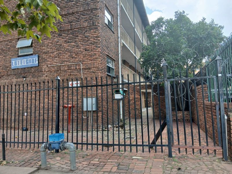 Exterior view of the Luttichof apartment building featuring a face brick facade, secure perimeter fencing with razor wire, and paved access area.