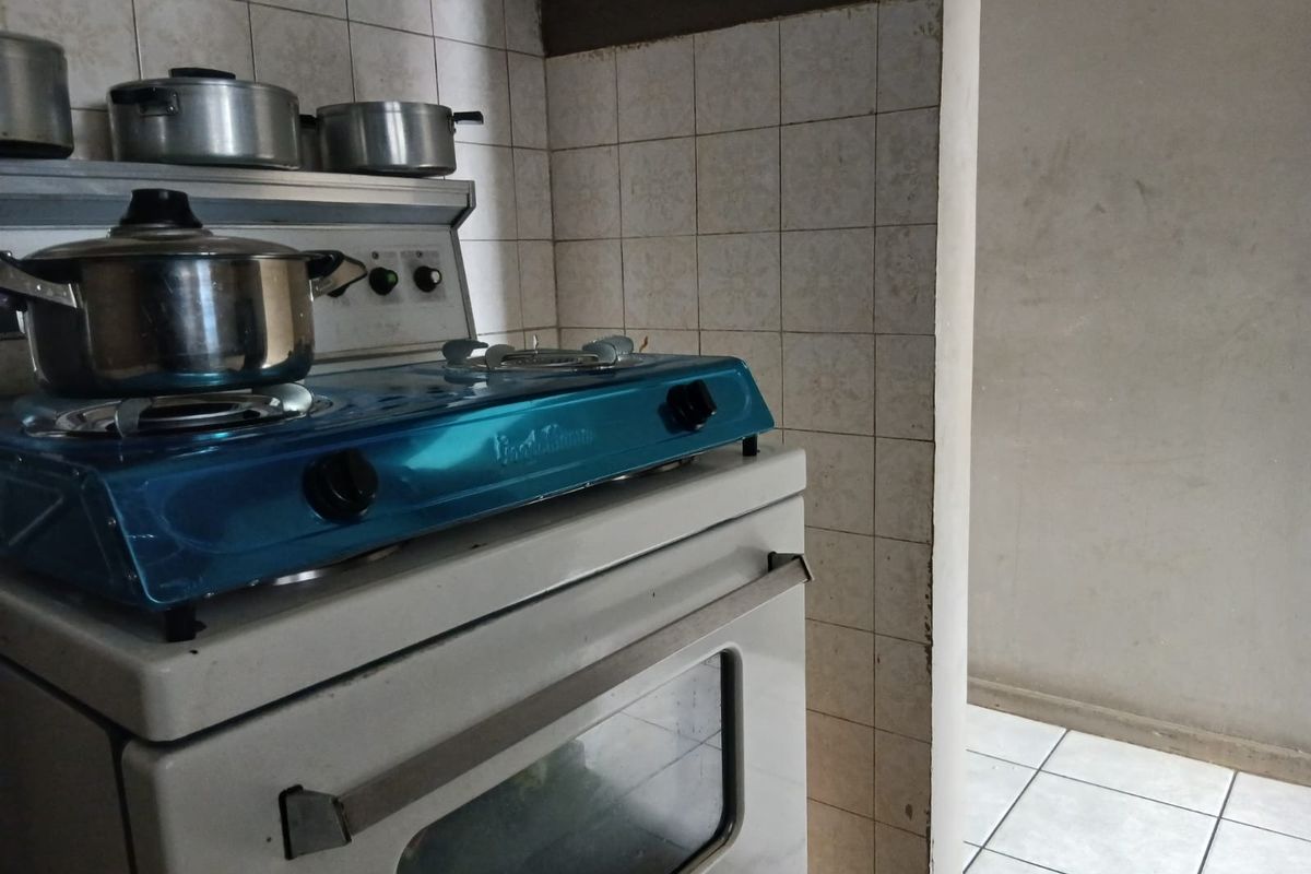 A dated kitchen area featuring a freestanding stove and ceramic wall and floor tiling, requiring cosmetic updates to modernize the space.