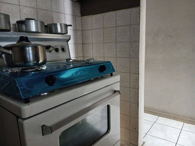 A dated kitchen area featuring a freestanding stove and ceramic wall and floor tiling, requiring cosmetic updates to modernize the space.