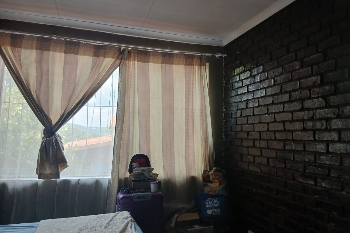 A bedroom featuring a dark exposed brick feature wall and large windows fitted with security bars.