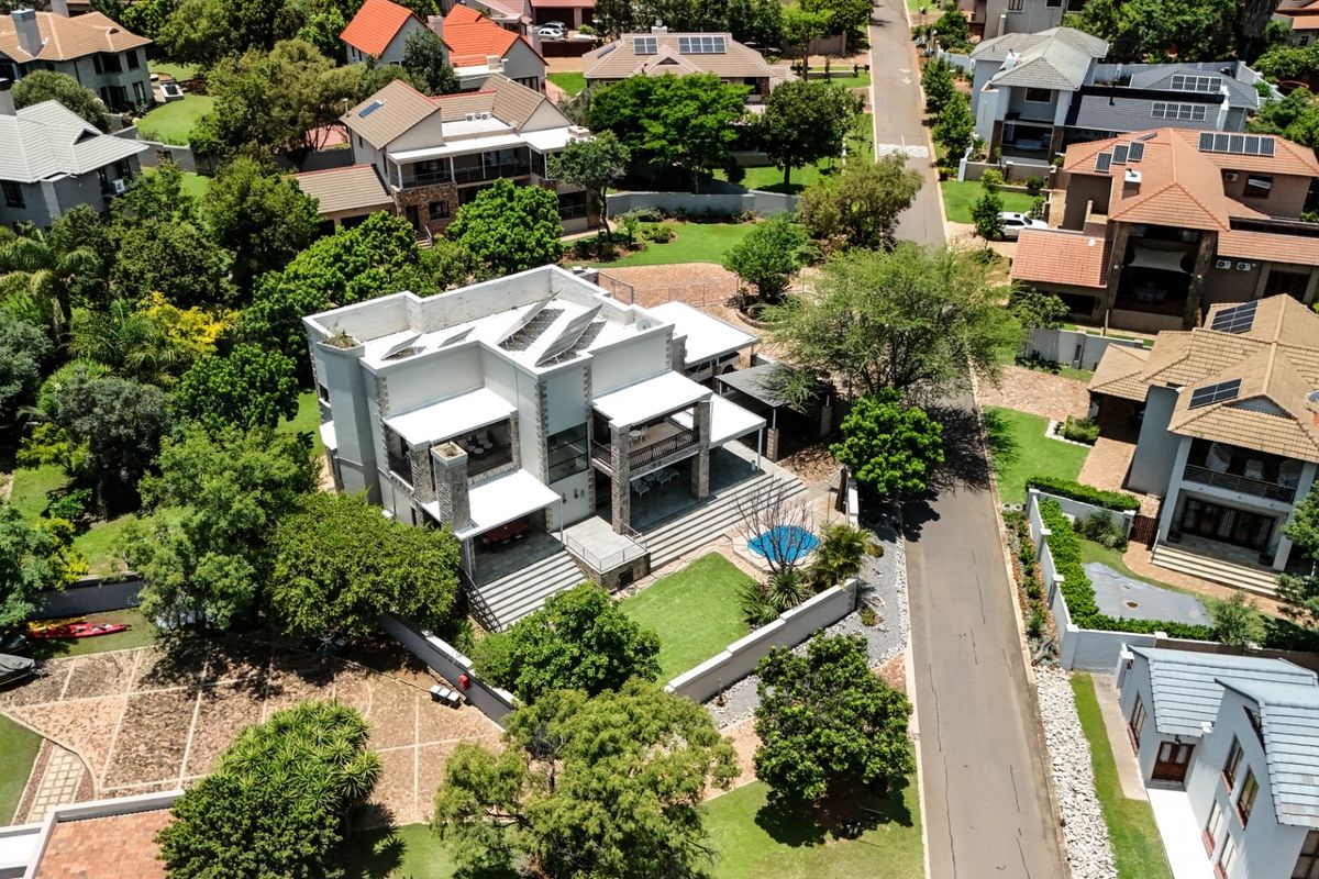 Aerial view of a modern residential property featuring a landscaped garden, swimming pool, covered patio, and solar panels on the roof.