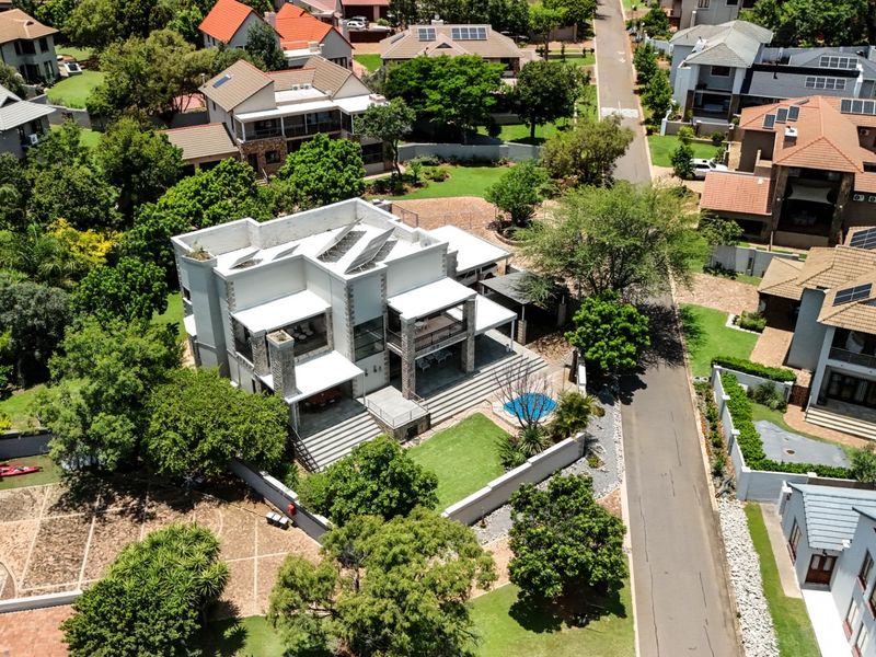 Aerial view of a modern residential property featuring a landscaped garden, swimming pool, covered patio, and solar panels on the roof.
