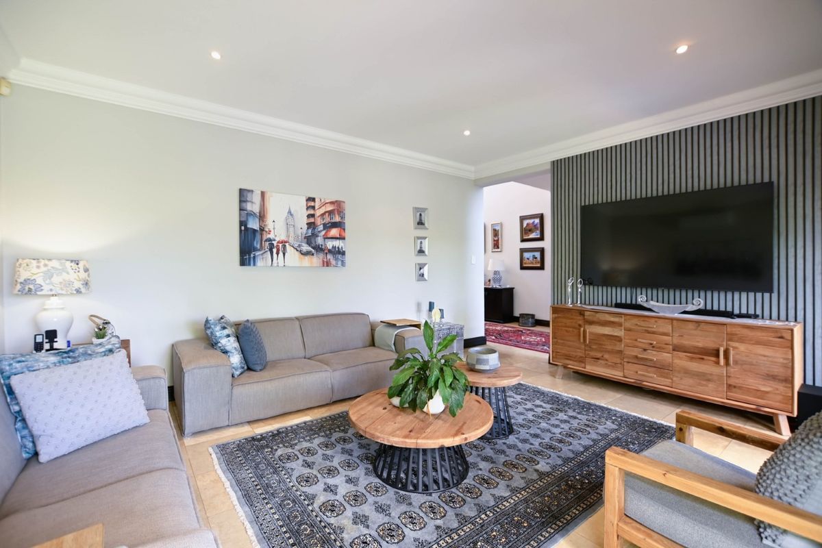 A well-maintained living room featuring a modern slatted timber feature wall, recessed downlighting, decorative crown molding, and neutral tiled flooring.