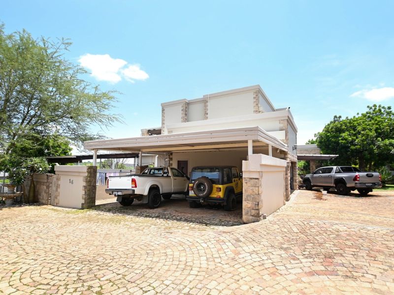 Front exterior view of the property featuring a paved driveway and a covered carport structure with stone-clad accents.