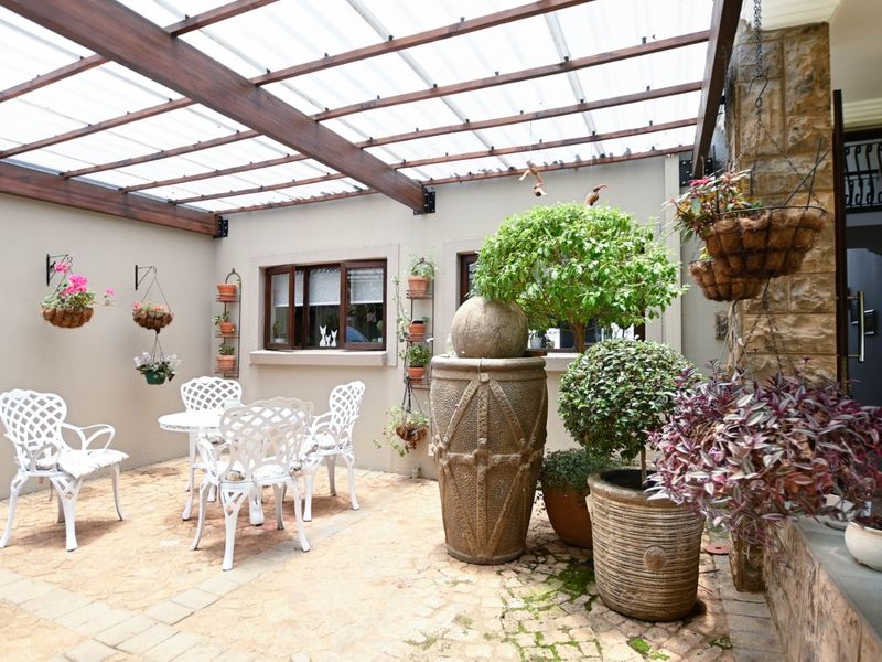 A covered outdoor patio area featuring a timber pergola with translucent roofing, stone wall accents, and paved flooring, creating a pleasant sheltered entertainment space.