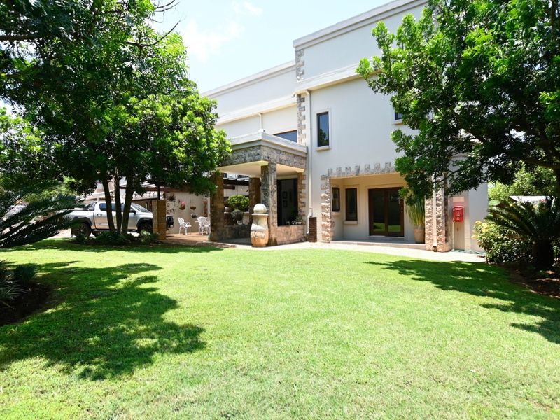 A well-maintained rear exterior view featuring a spacious lawn, stone-clad architectural details, and a covered patio area.