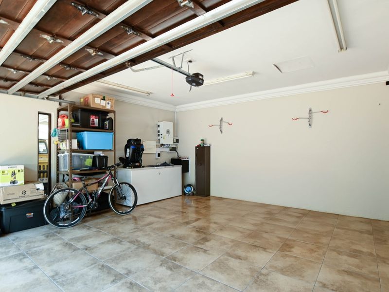 Spacious double garage featuring tiled flooring, timber sectional door, and wall-mounted storage hooks, providing ample space for vehicles and utility storage.