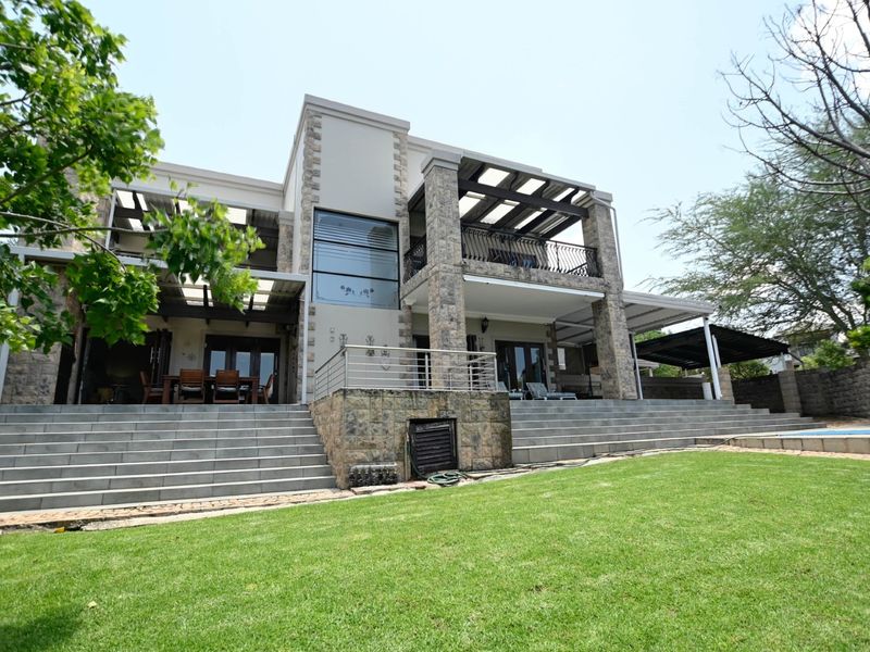 Rear view of a multi-story residence featuring stone cladding, expansive covered patios, balconies with metal railings, and wide concrete stairs leading to a landscaped garden.