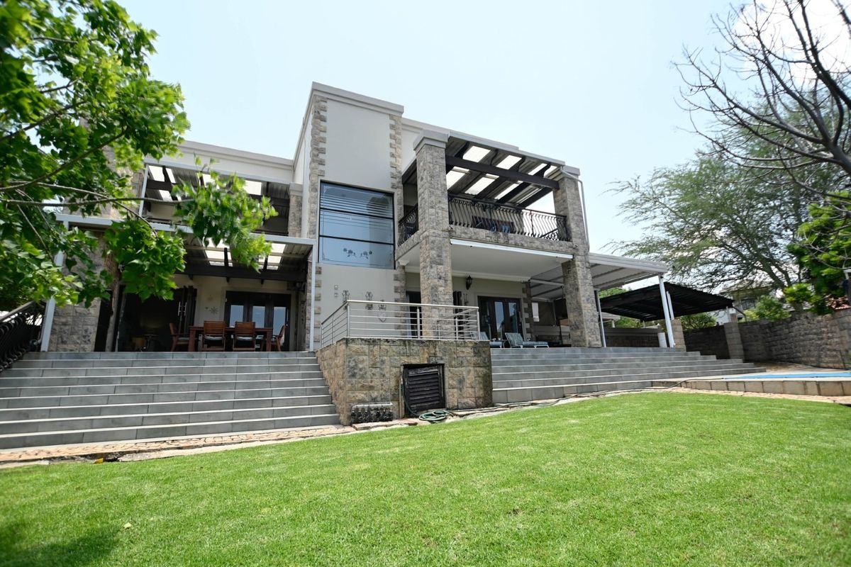 Rear view of a multi-story residence featuring stone cladding, expansive covered patios, balconies with metal railings, and wide concrete stairs leading to a landscaped garden.