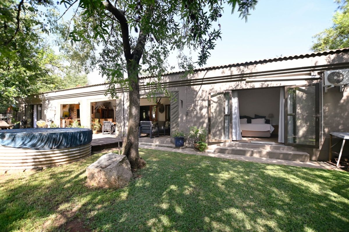 Rear view of the property featuring a landscaped garden, a corrugated metal water tank, and multiple sets of french doors leading into the home.