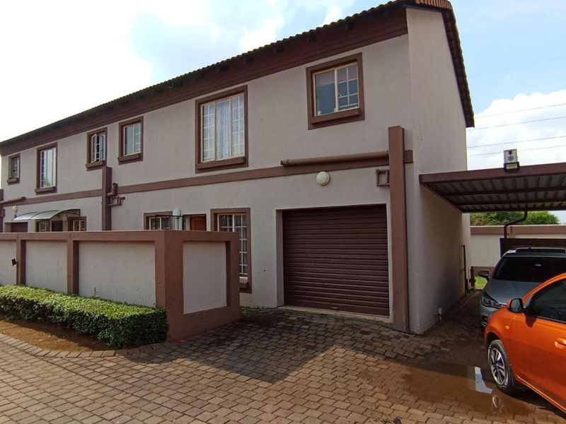 Front elevation of a double-storey townhouse featuring a paved driveway, integrated garage, and a covered carport area.