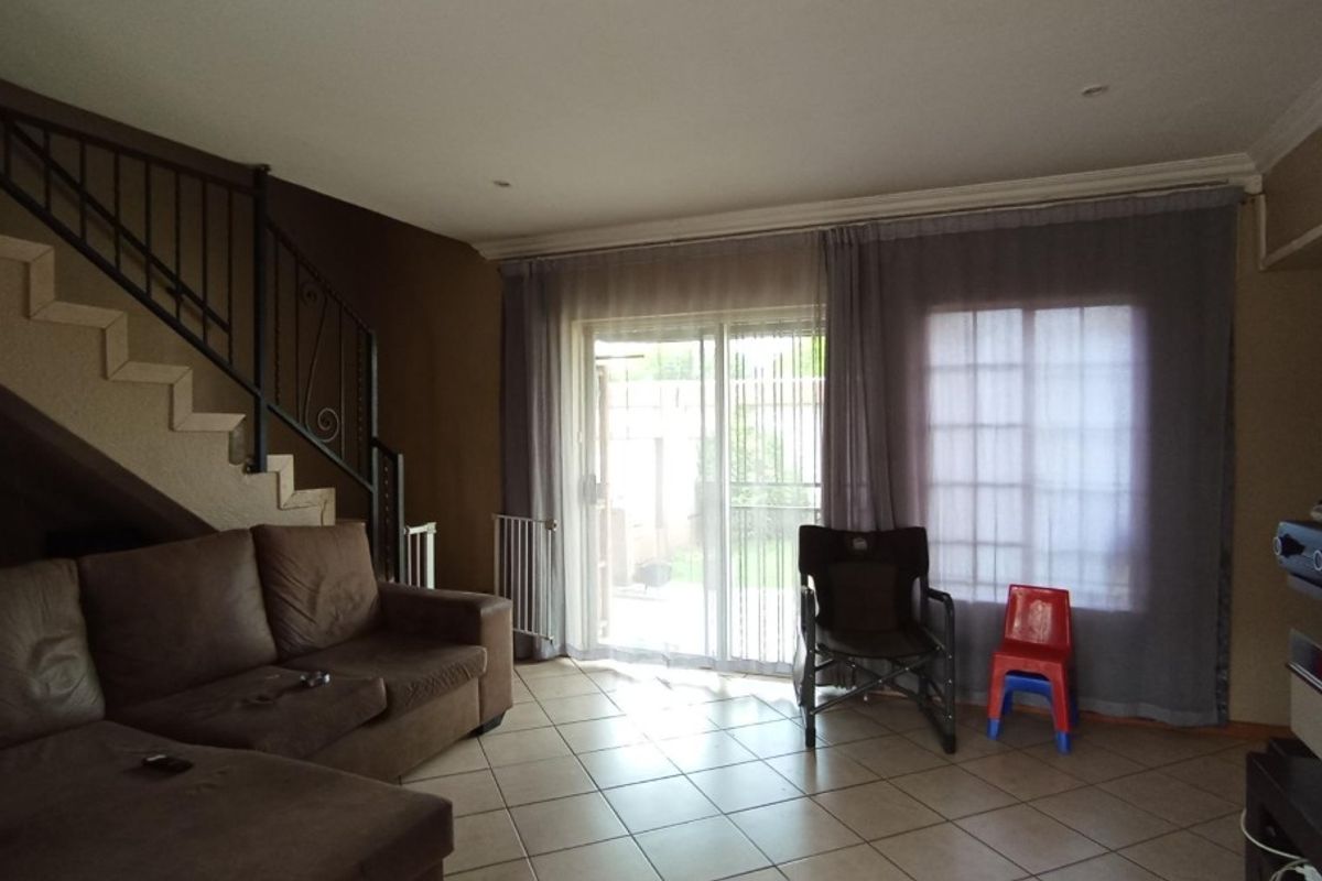 Spacious living room featuring tiled flooring, a staircase with a wrought iron balustrade, and sliding glass doors providing access to the outdoor area.