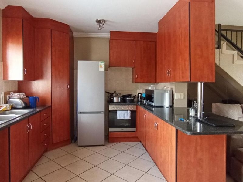 A functional kitchen featuring warm-toned laminate cabinetry, granite countertops, a breakfast bar, and tiled flooring, conveniently located adjacent to the staircase.