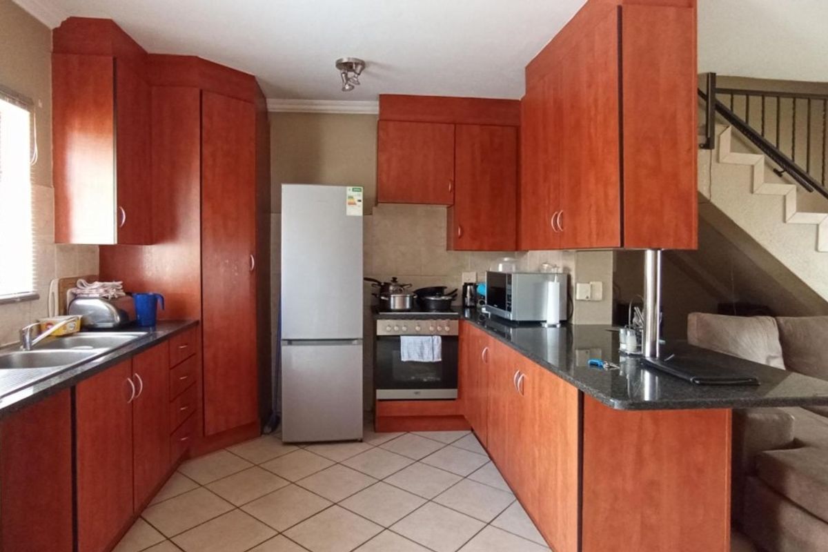 A functional kitchen featuring warm-toned laminate cabinetry, granite countertops, a breakfast bar, and tiled flooring, conveniently located adjacent to the staircase.