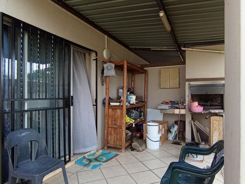 Covered patio area featuring a built-in braai, tiled flooring, and direct access to the interior through a sliding security door.