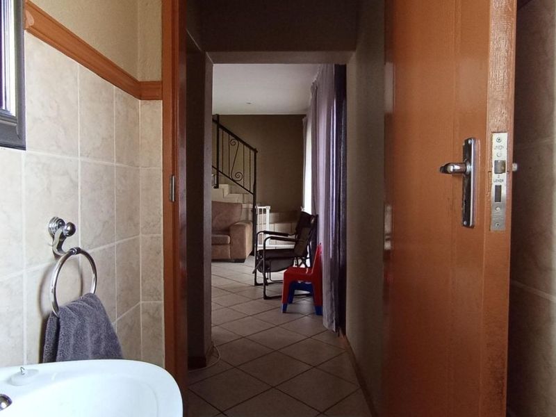 A functional bathroom featuring ceramic wall and floor tiling, a pedestal basin with chrome fixtures, and a view through to the adjacent living area.