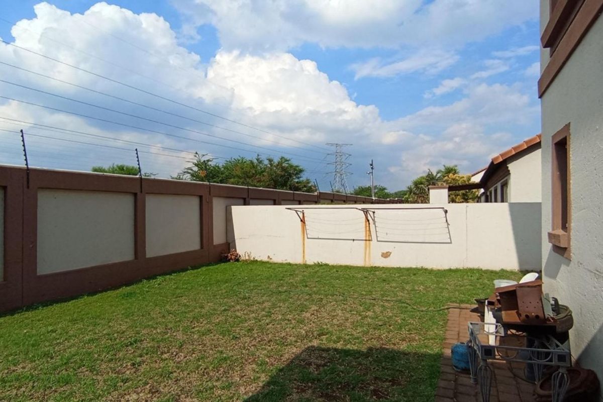 A private rear garden featuring a lawn, paved area, and perimeter wall with electric fencing and a wall-mounted washing line.
