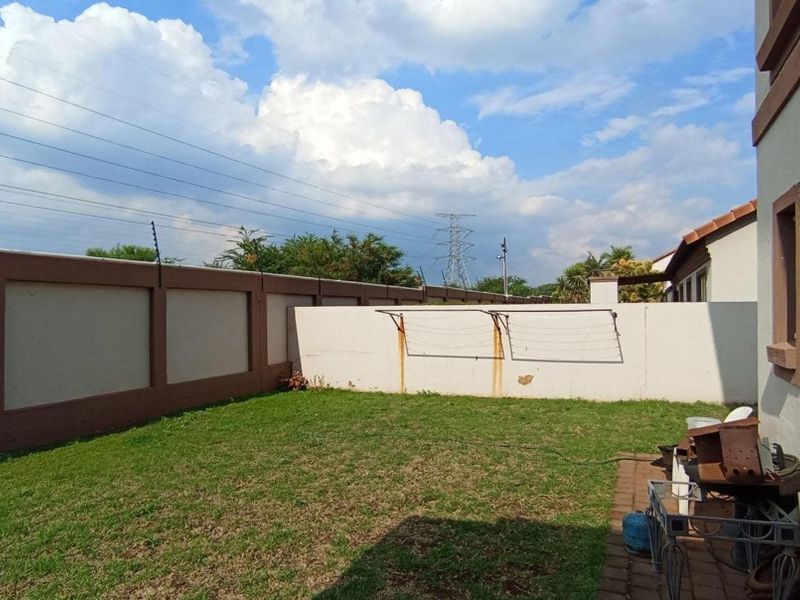 A private rear garden featuring a lawn, paved area, and perimeter wall with electric fencing and a wall-mounted washing line.