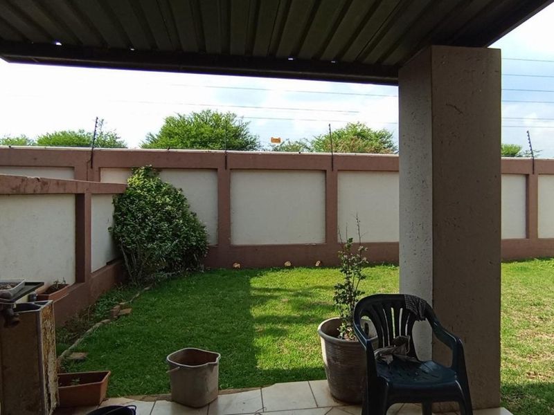 Covered patio area featuring a built-in braai, overlooking a private garden enclosed by a perimeter wall with electric fencing.