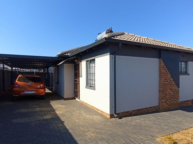 A well-maintained single-story house featuring a paved driveway, integrated carport, solar water heating system, and modern exterior finishes with brick accents.